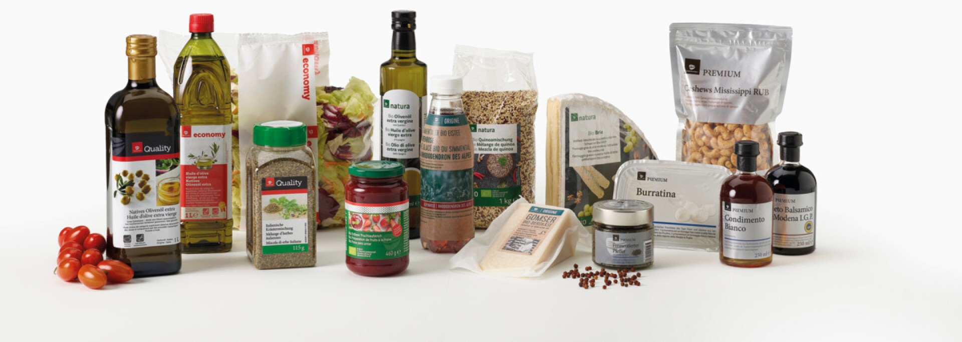 Eine Auswahl verschiedener italienischer Lebensmittel, darunter Olivenöl, Pasta, Käse, eingelegtes Gemüse, Soßen, Balsamico-Essig, Gewürze und abgepackte Nüsse, alle in einer Reihe auf weißem Hintergrund angeordnet.