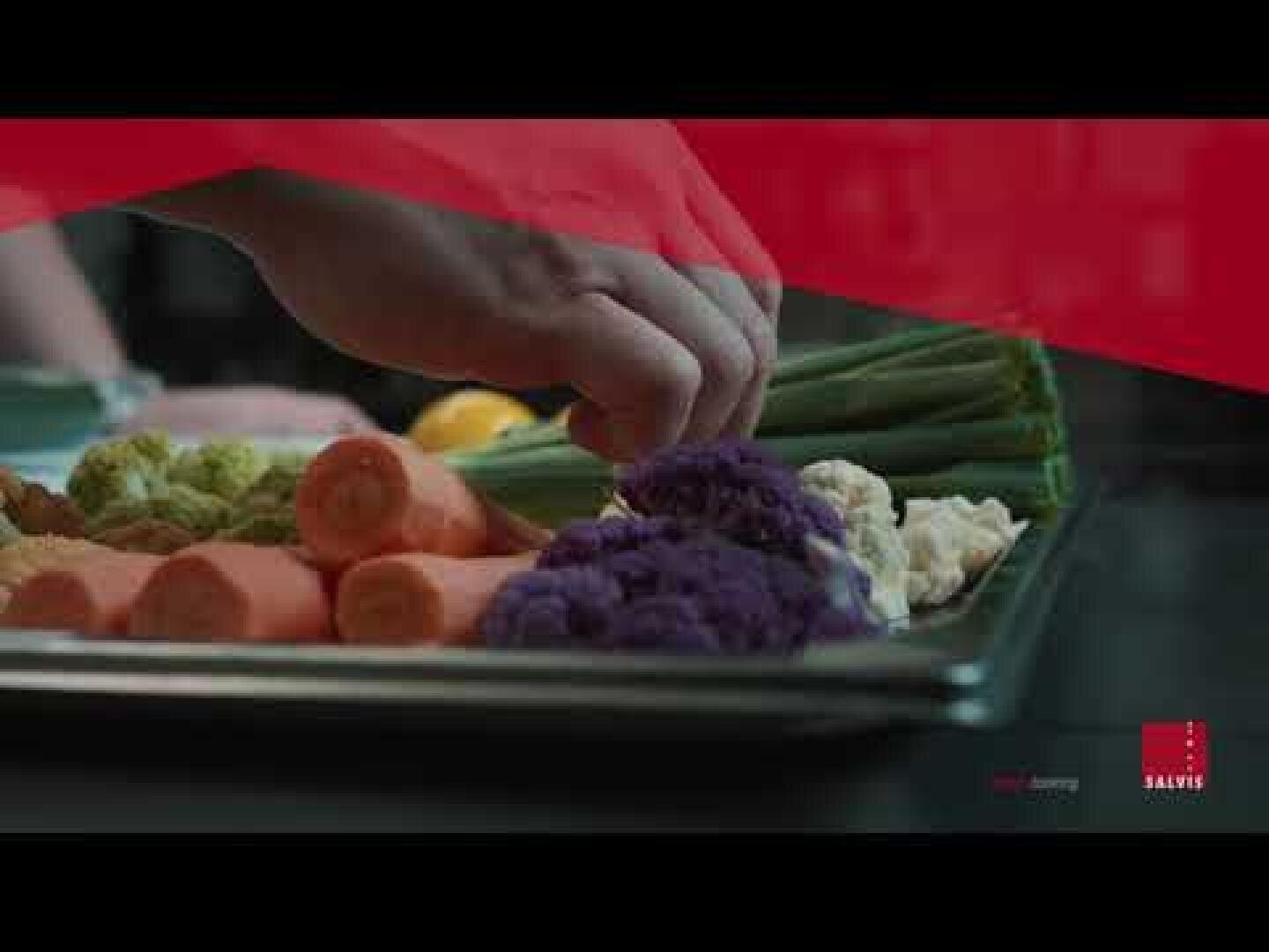 Une main tend la main vers des légumes frais, dont des carottes, du chou-fleur et des oignons nouveaux, disposés sur un plateau en métal. L'image est superposée en rouge et comporte un petit logo dans le coin inférieur droit.