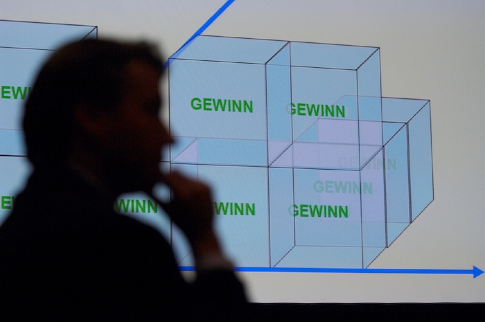 Die Silhouette einer Person vor einem Bildschirm, auf dem transparente 3D-Würfel mit der Aufschrift „GEWINN“ auf weißem Hintergrund angezeigt werden.